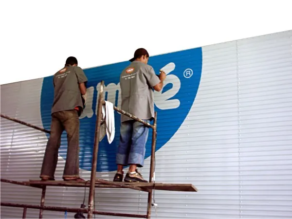 Dois instaladores aplicando o logotipo numa fachada, sobre andaime